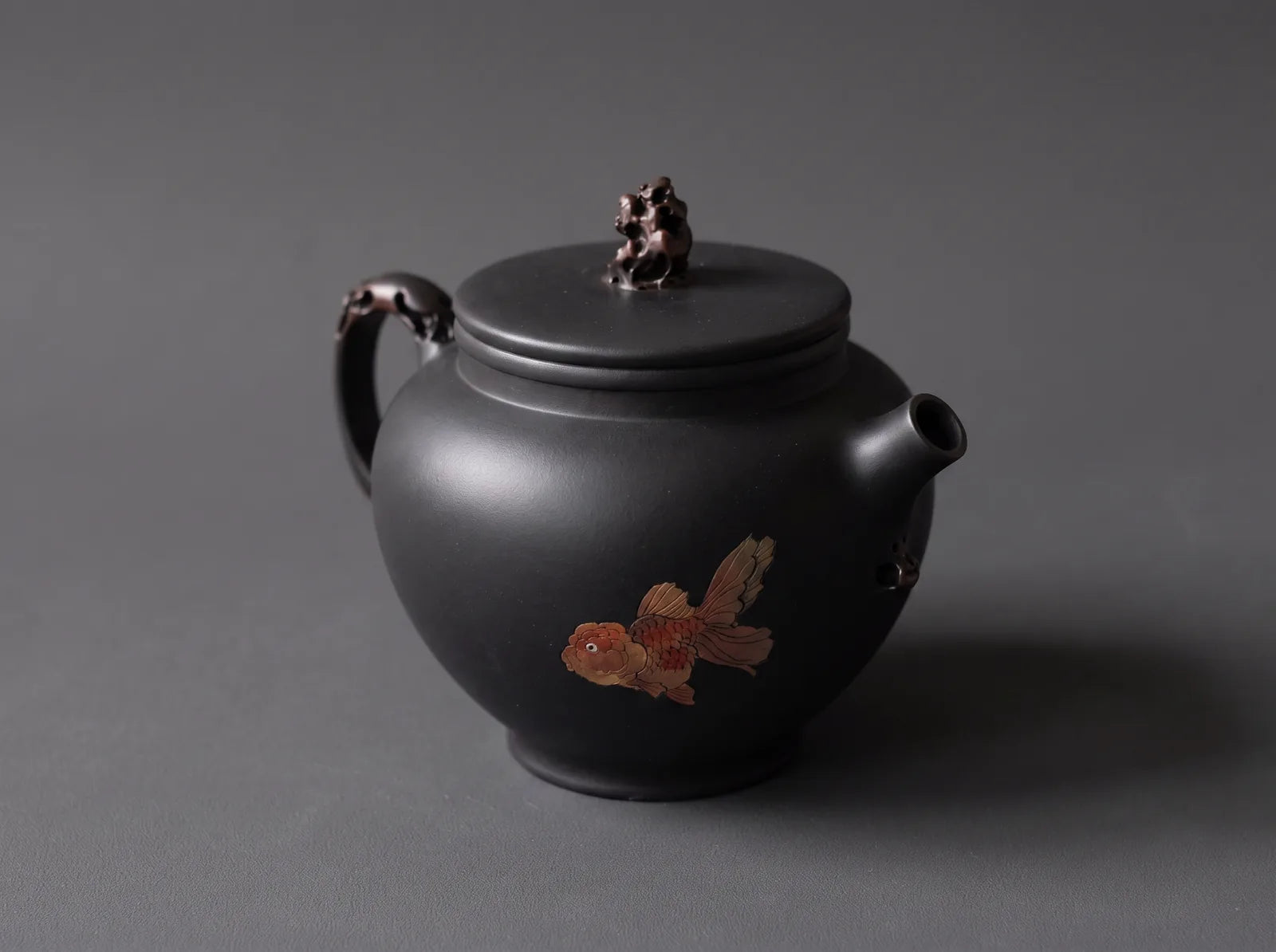 Jianshui – Black Duozhi Teapot with Goldfish in an editorial setting