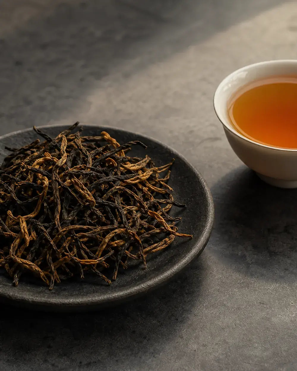 Whole-leaf Chinese black tea beside an amber tea cup
